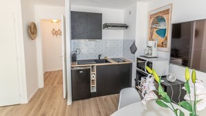A compact kitchen with a dishwasher, a microwave, and a small refrigerator. There is a white wall with a decorative poster and a white door leading to another room. - La Naïade - à 200m de la plage (Carnac)