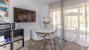 A dining area with a white table, four chairs, a vase with flowers, a microwave, and a television on the wall. - La Naïade - à 200m de la plage (Carnac)