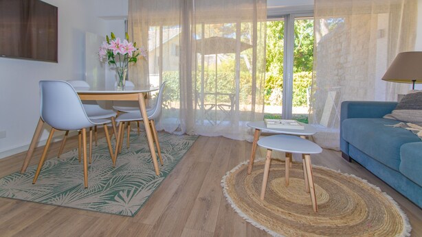 A modern living room with a dining area, a sofa, and a TV mounted on the wall. - La Naïade - à 200m de la plage (Carnac)