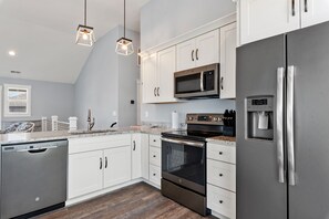 Enjoy cooking in this well-equipped kitchen with a refrigerator, microwave, and oven, plus a granite countertop and pendant lights.