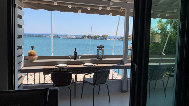A balcony with a view of the sea, a table with two wine glasses, a bottle, and a lantern. - Pythagorion Harbour Residence (Pythagoreio)