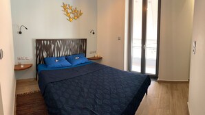 A bedroom with a bed, two nightstands, a wall-mounted light fixture, and a decorative wall piece. - Pythagorion Harbour Residence (Pythagoreio)