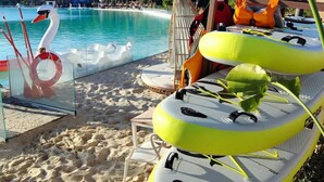 Une vue sur la plage avec une piscine à l’eau cristalline, un cygne en décoration et des jeux d’eau gonflables.