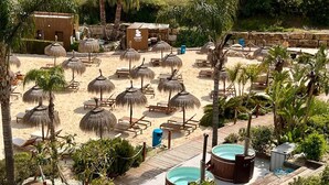 Un complexe hôtelier de bord de mer doté de parasols en chaume, de chaises longues en bois, d’une piscine et d’un centre de massage.