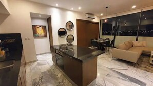 Una cocina moderna con una isla central, un comedor con mesa y sillas, y un sofá en una sala de estar con vista a la ciudad.