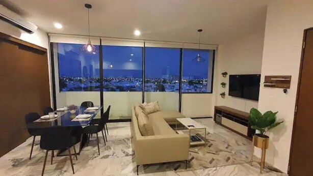 Una sala de estar moderna con un ventanal grande, un sofá, una mesa de comedor y un televisor.