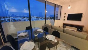 Un comedor con una mesa de vidrio dispuesta para cuatro personas, un sofá y un televisor montado en la pared.