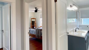 Et moderne køkken med en central ø, et spiseområde med bord og stole, samt et soveværelse med seng og ventilator.