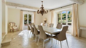 Un comedor con una gran mesa, seis sillas, una araña y ventanas amplias con cortinas.