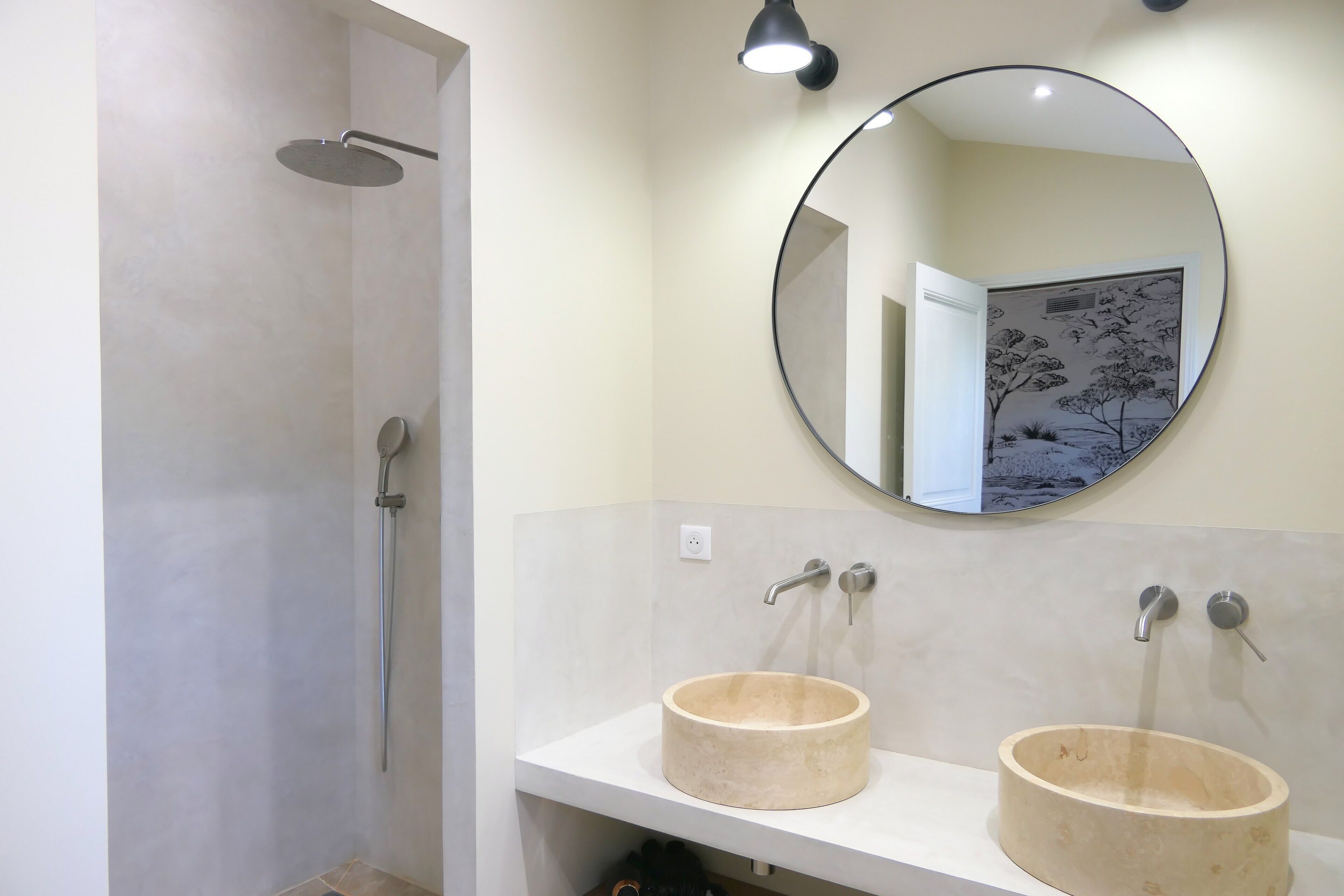 A bathroom with a shower, two sinks, and a round mirror.