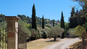 Un camino de grava que conduce a una entrada con puerta, con un letrero que dice 'Bastide des Platries'.