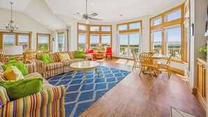 A spacious living room with a high ceiling, large windows, and a ceiling fan. - Soundfront Dog Friendly Home w/ Pool, Hot Tub, Elevator, Private Sound Boardwalk (Avon)