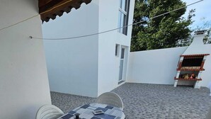 Un patio con una mesa para dos, una parrilla y una pared blanca.