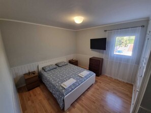 A bedroom with a bed, bedside tables, a dresser, a flat-screen TV, and a window with curtains.