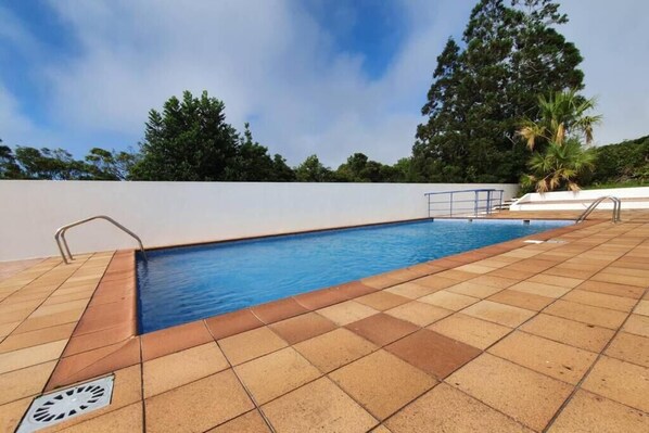 A swimming pool with a tiled deck, metal handrails, and a drain cover.