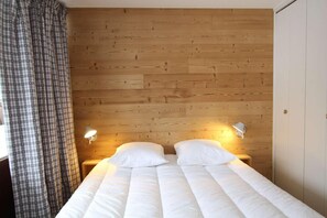 Un lit avec une literie blanche, deux lampes de chevet et une tête de lit en bois.