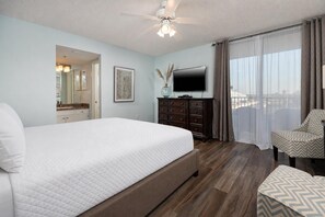 A hotel room with a large bed, a dresser, a television, and a balcony with curtains. - Relax with Gulf Views at Phoenix East 201 Escape (Orange Beach)