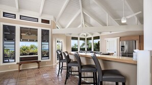 A kitchen with a bar area, large windows, and a ceiling fan. - Pineapple House: Ocean View Home in Keauhou Estates w/ Private Hot Tub, BBQ & AC (Kailua Kona)