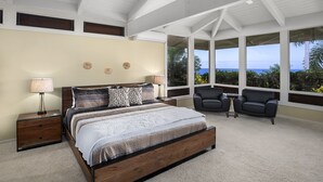 A bedroom with a large bed, two nightstands, a chair, and a view of the ocean. - Pineapple House: Ocean View Home in Keauhou Estates w/ Private Hot Tub, BBQ & AC (Kailua Kona)