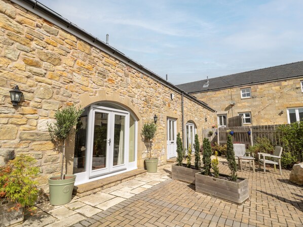 A stone building with a paved patio, outdoor seating, and potted plants. - Calm Skies (Berwick-upon-Tweed)