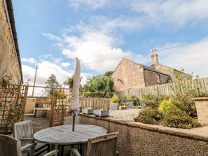 A rustic outdoor seating area with a round wooden table and chairs, surrounded by a stone wall and a wooden fence. - Calm Skies (Berwick-upon-Tweed)