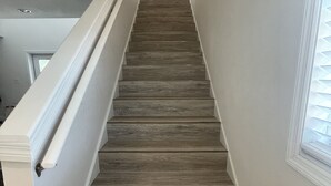 A wooden staircase with white walls and a window on the right. - Large 2 Bedroom Suite with Secret Garden—5 min from downtown! (St. Petersburg)