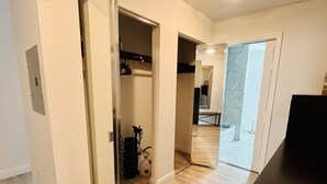 A hallway with a wooden floor, a closet with hanging clothes, and a door leading to a bathroom with a marble floor. - Large 2 Bedroom Suite with Secret Garden—5 min from downtown! (St. Petersburg)