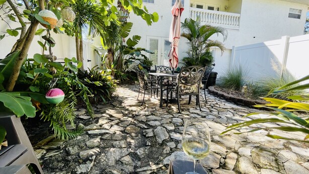A patio area with stone flooring, outdoor furniture, and a glass of white wine. - Large 2 Bedroom Suite with Secret Garden—5 min from downtown! (St. Petersburg)