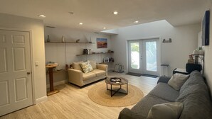 A spacious living room with a beige sofa, a grey sofa, and a coffee table. There are shelves with decorative items and a door leading outside. - Large 2 Bedroom Suite with Secret Garden—5 min from downtown! (St. Petersburg)