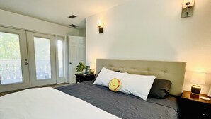 A bedroom with a large bed, a nightstand, a wall-mounted lamp, and a door leading to a balcony. - Large 2 Bedroom Suite with Secret Garden—5 min from downtown! (St. Petersburg)