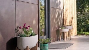 A modern building exterior with large windows, a wooden deck, and potted plants.