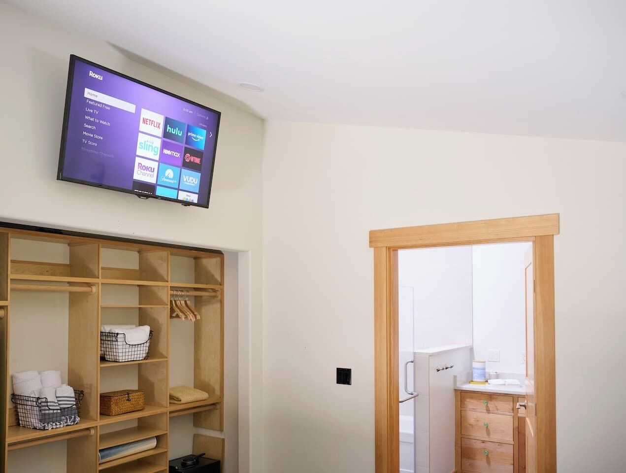 A room with a TV displaying streaming services, a wooden wardrobe, and a bathroom visible through an open door.