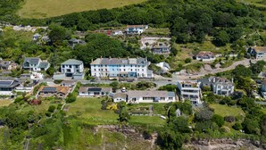 Vue aérienne d’une zone résidentielle côtière, avec des maisons, une plage et une côte rocheuse.