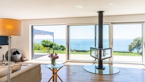 Un salon moderne comprenant un canapé, une table en verre, une cheminée et une grande porte-fenêtre coulissante donnant sur la mer.