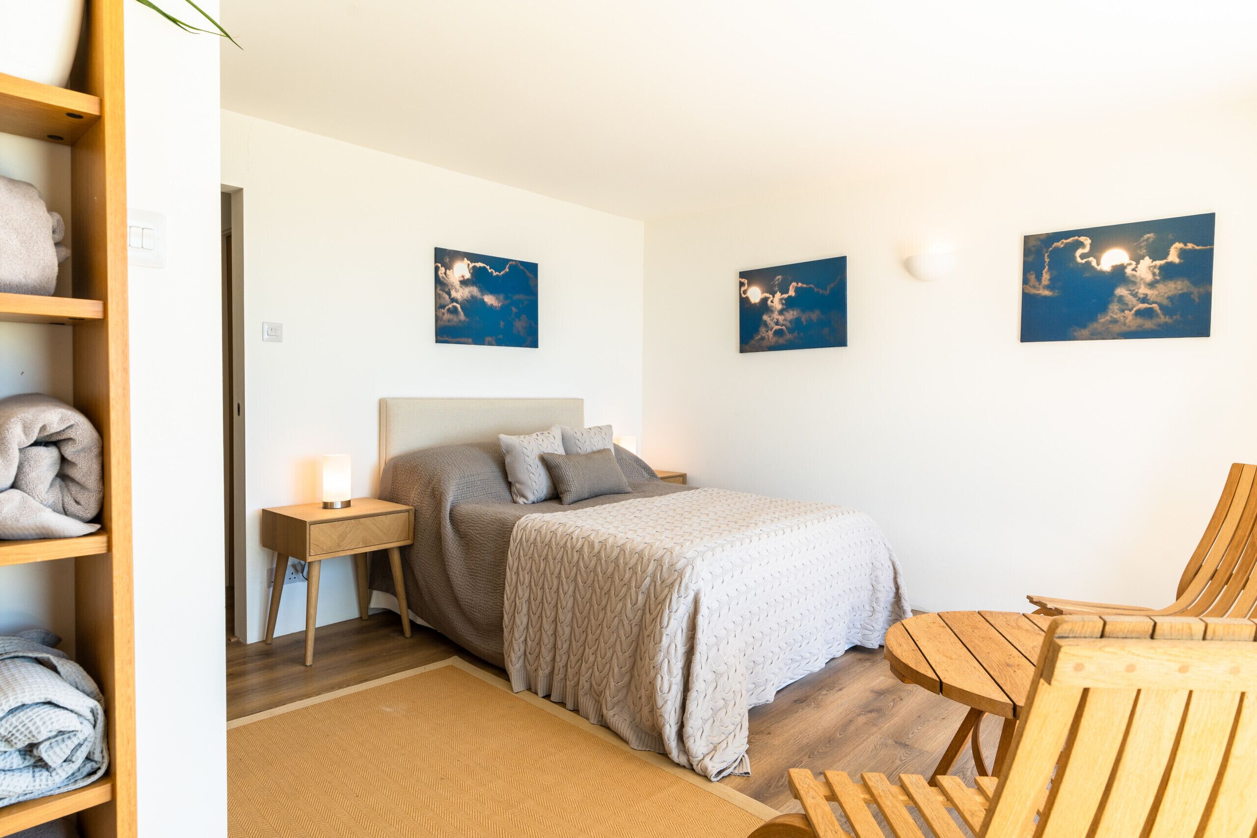 Un dormitorio con cama, mesita de noche, una silla y una repisa con toallas.
