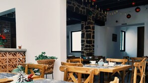Un comedor con mesas y sillas de madera, plantas en macetas y una pared de piedra.
