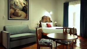 Una habitación de hotel con cama, sofá, mesa de comedor y un cuadro grande en la pared.
