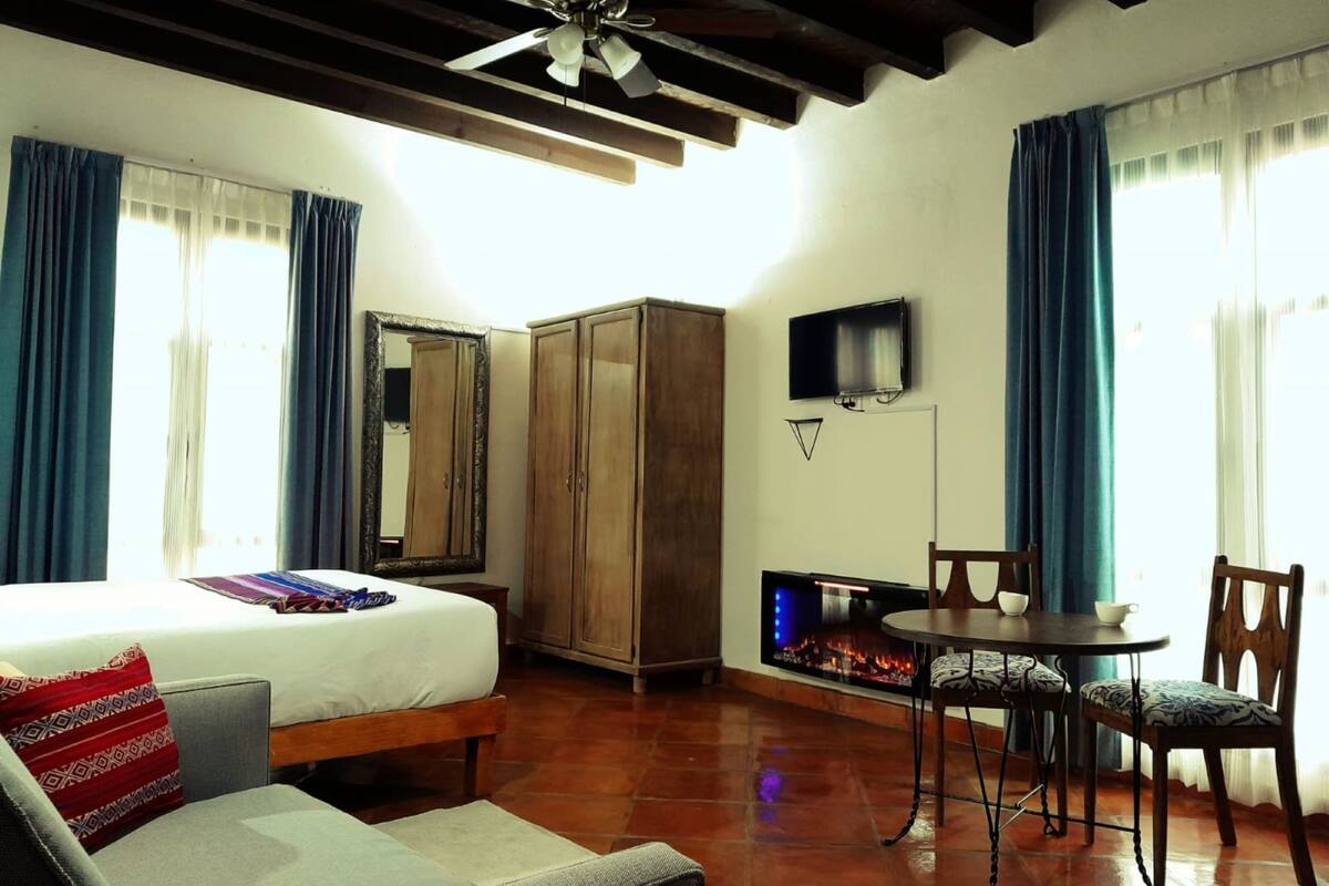 A hotel room with a bed, a sofa, a dining table with chairs, a TV, and a wardrobe.