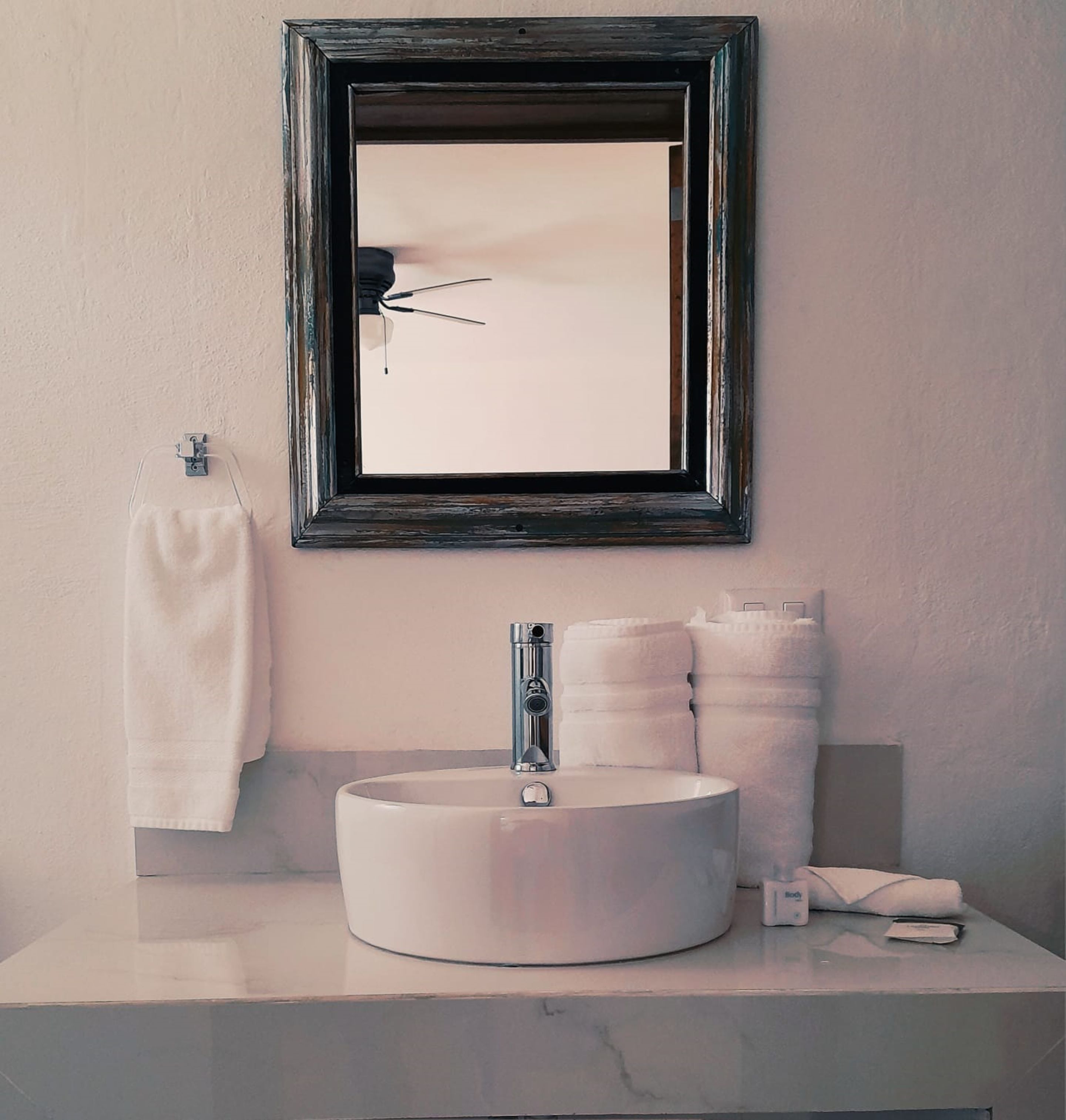A bathroom with a round sink, a mirror, and a towel rack.