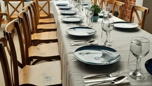 Una mesa de comedor lista con platos, cubiertos y vasos, rodeada de sillas de madera.