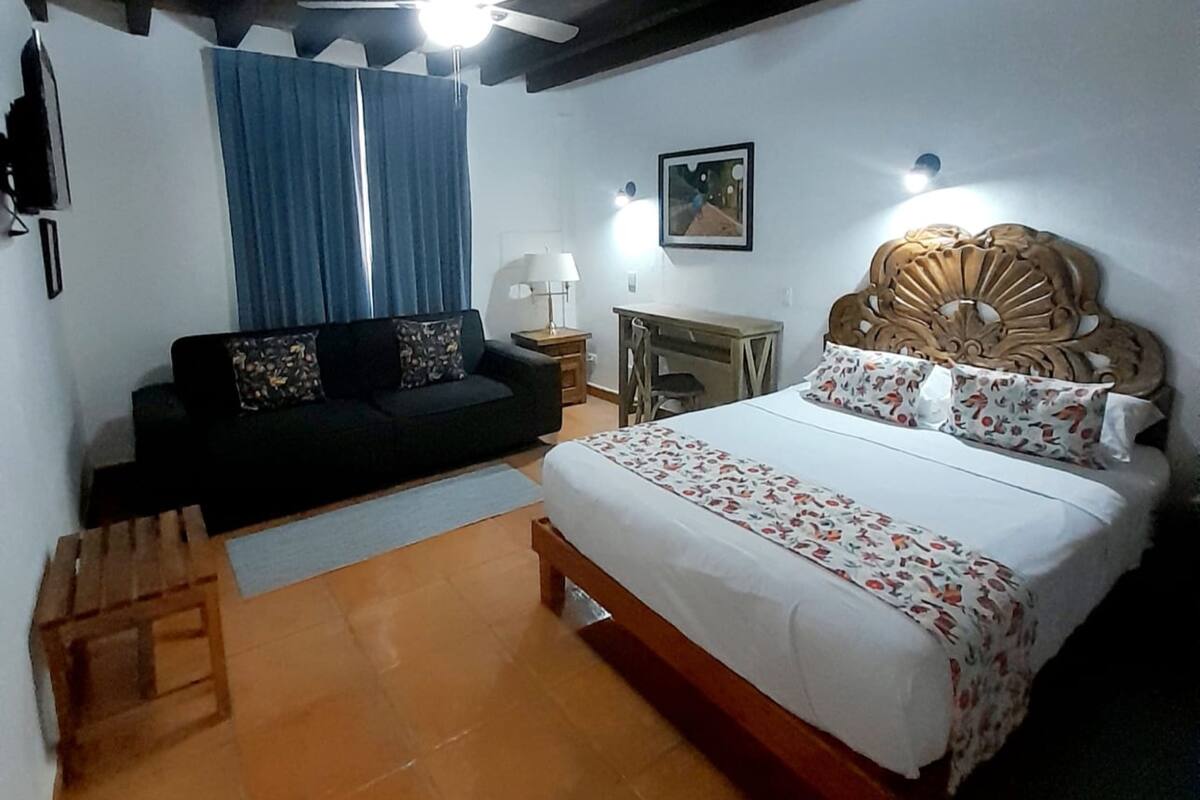 A bedroom with a bed, a sofa, a nightstand, a ceiling fan, and a window with curtains.