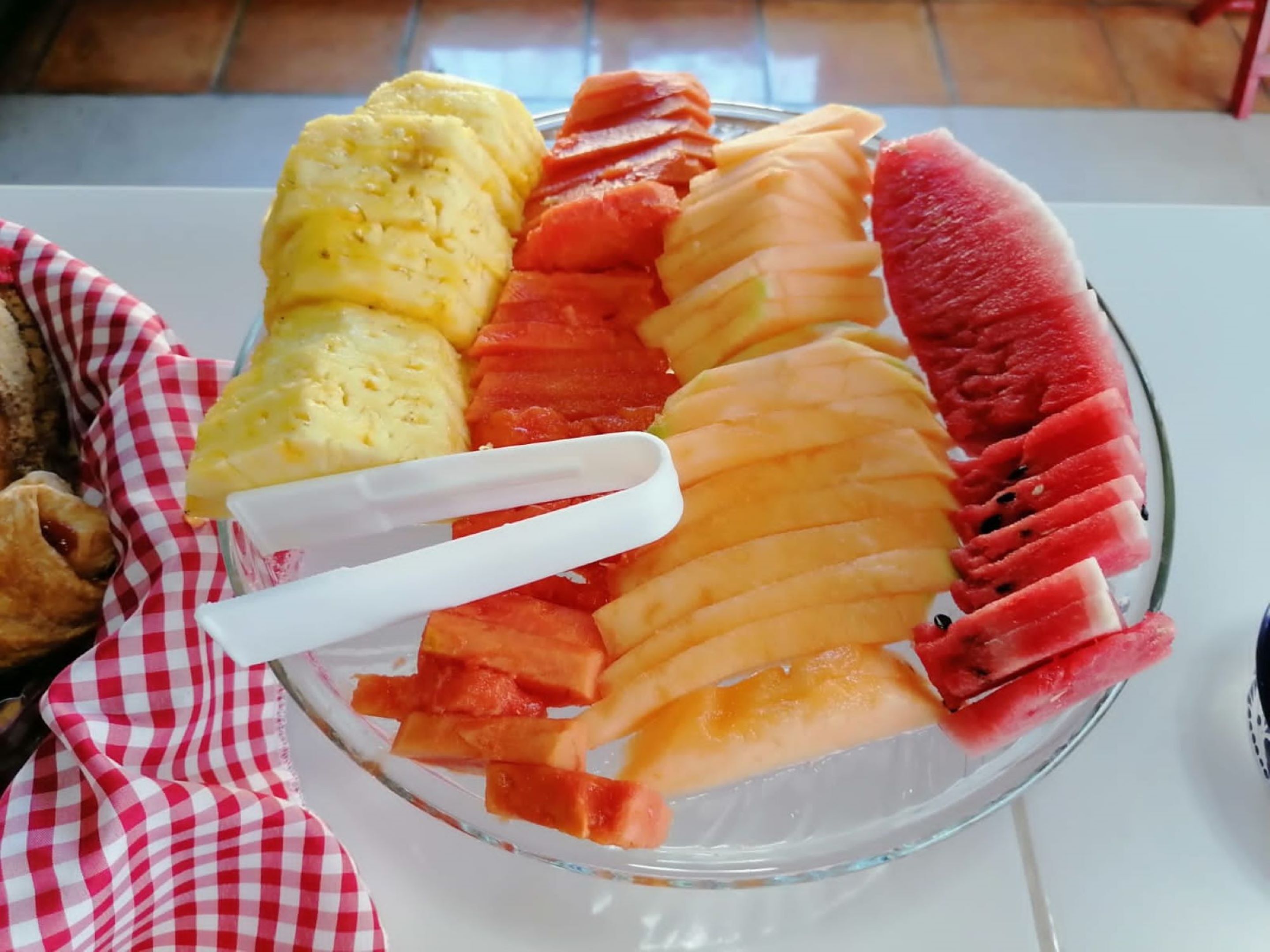 A glass bowl containing sliced watermelon, cantaloupe, and pineapple on a table.