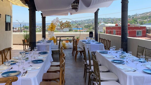 Un área de comedor al aire libre con manteles blancos, sillas doradas y un letrero que dice 'Nuestra Boda'.