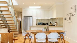 A modern kitchen with white cabinets, a stainless steel refrigerator, and a dining area with a wooden table and chairs. - Farrah - Designer, Three Bedroom Carlton Residence (Carlton)