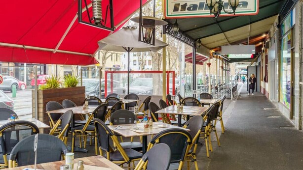 An outdoor cafe with tables and chairs under a red awning, a gas station sign in the background, and a sidewalk with pedestrians. - Farrah - Designer, Three Bedroom Carlton Residence (Carlton)