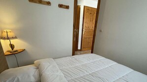A bedroom with a bed, pillows, a bedside table with a lamp, and a wooden door. - Ground floor, view mountain, terrace, tv, ski locker, 29m², Praz sur Arly (Praz-sur-Arly)