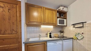 A compact kitchen with wooden cabinets, a microwave, a dishwasher, and a tiled backsplash. - Ground floor, view mountain, terrace, tv, ski locker, 29m², Praz sur Arly (Praz-sur-Arly)