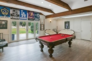 A pool table in a room with a view of a golf course, a pool table, and a door leading outside.