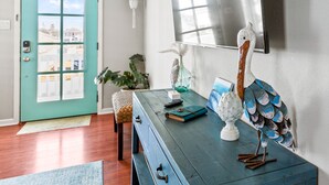 Una habitación con puerta verde azulada, un banco de madera, un aparador azul y una escultura decorativa de pájaro.