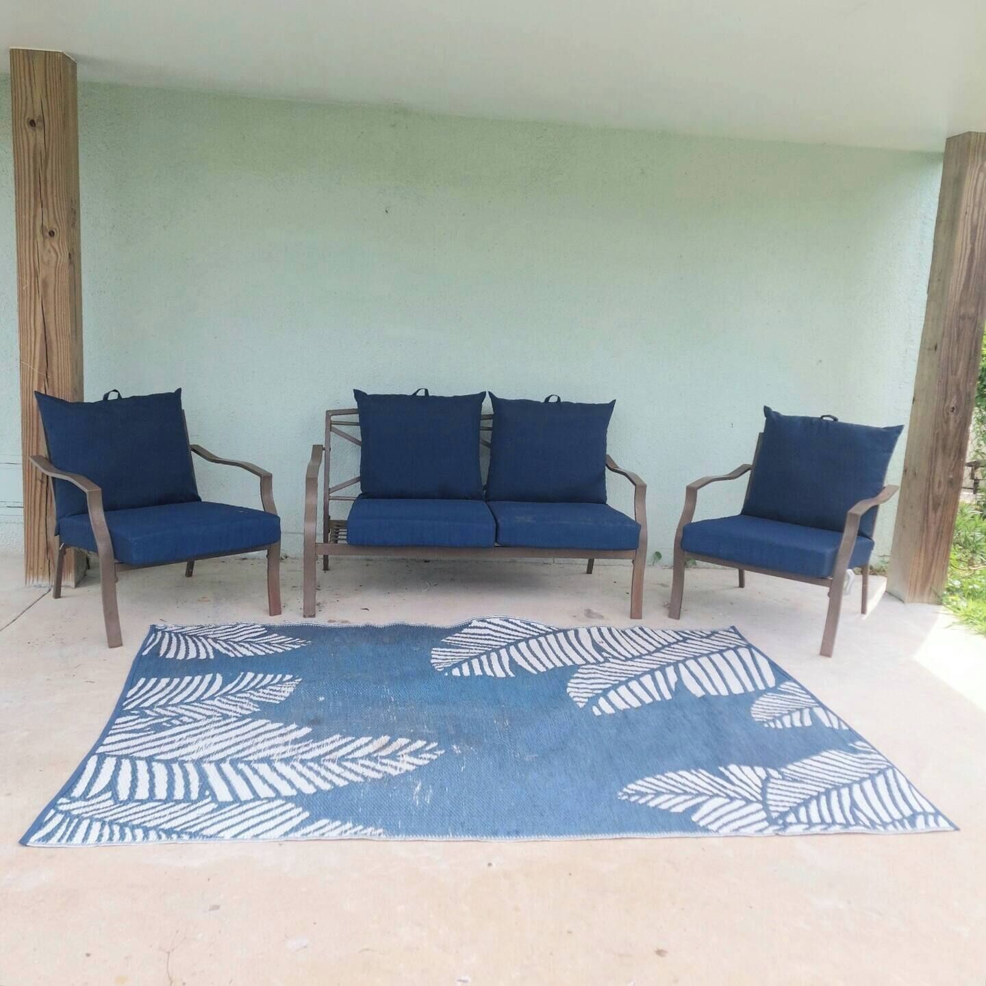 Un patio cubierto con tres sillas azules acolchadas y una alfombra estampada.
